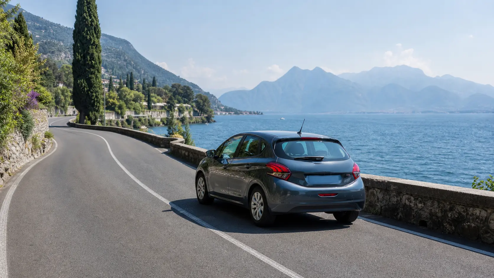 Rental car on a lakeside road beside Lake Garda with Italian Alps behind
