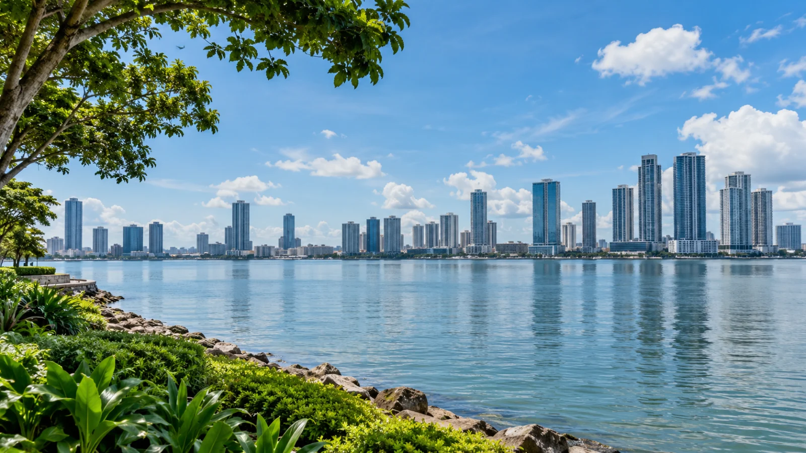 Modern waterfront skyline seen across calm water from a leafy shore