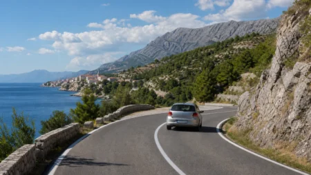 Car on a winding coastal road beneath rocky mountains