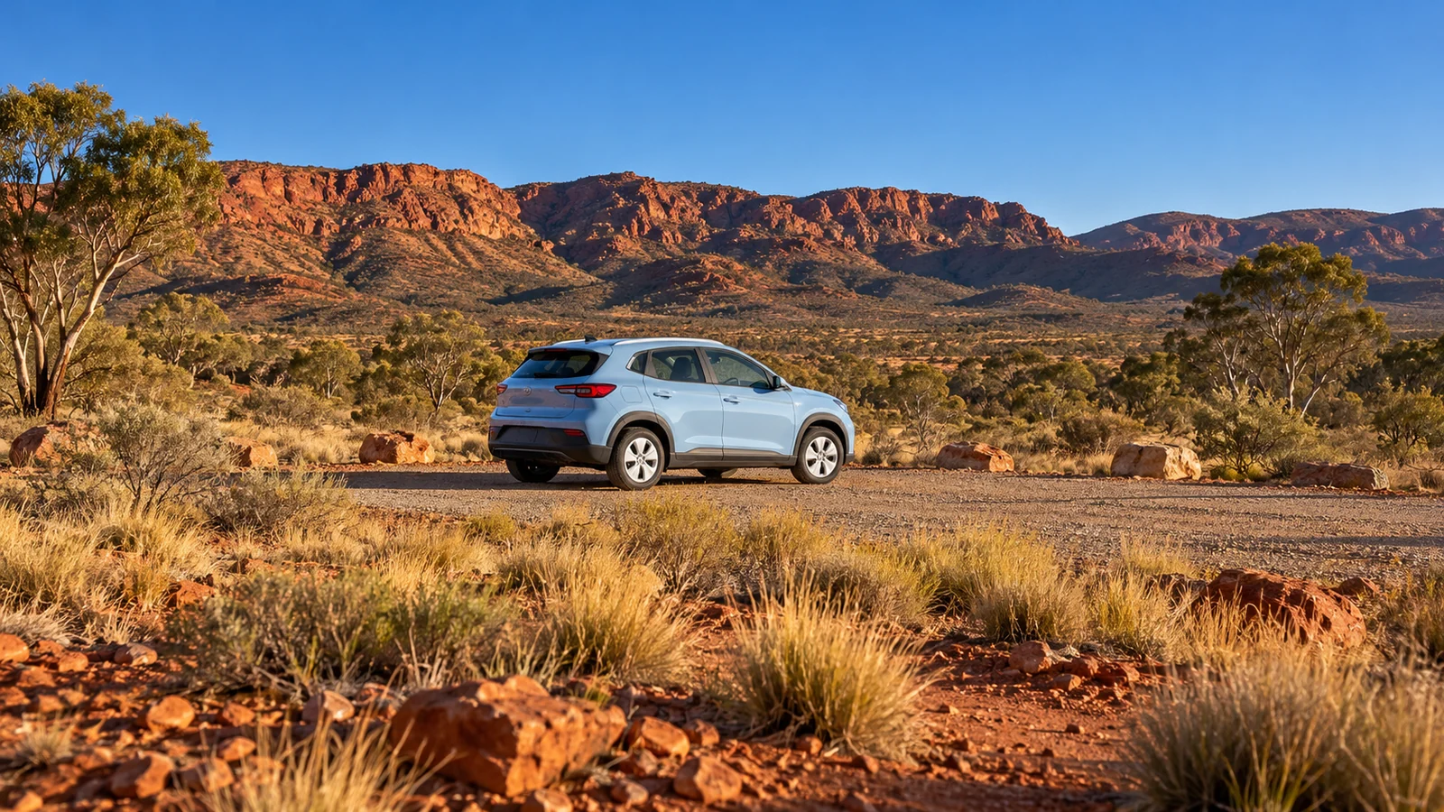 Pale-blue car at a gravel turnout beneath red-rock ranges