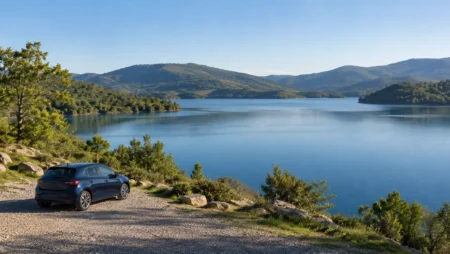 Blue car parked at a gravel overlook above a lake and wooded hills